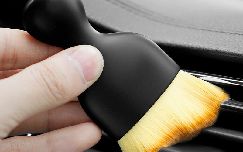 The gap brush held in one hand, sweeping along the slats of a car air vent.
