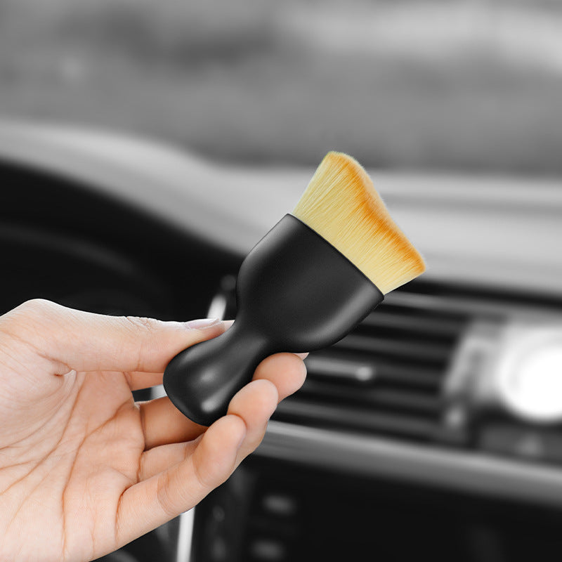 The gap brush held in one hand in front of a car dashboard and its air vents.