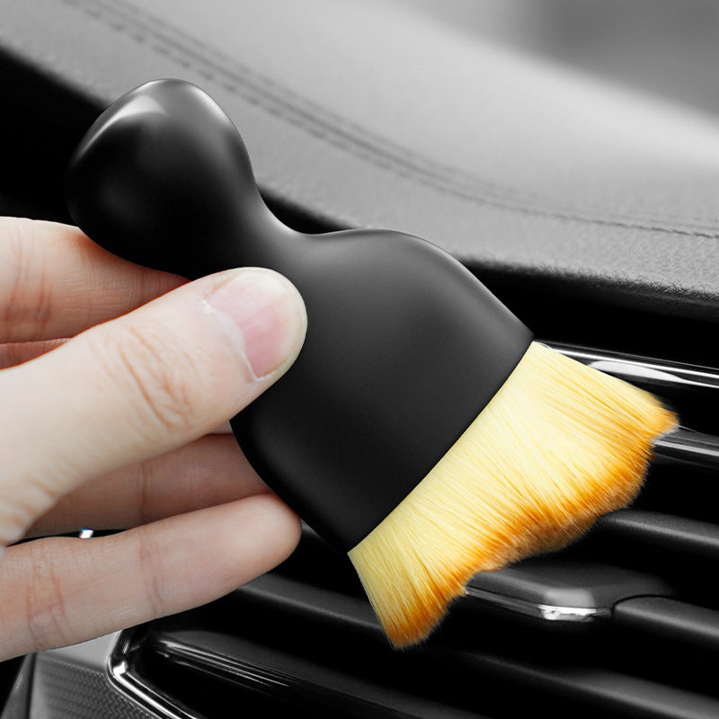 The gap brush held in one hand, sweeping along the slats of a car air vent.