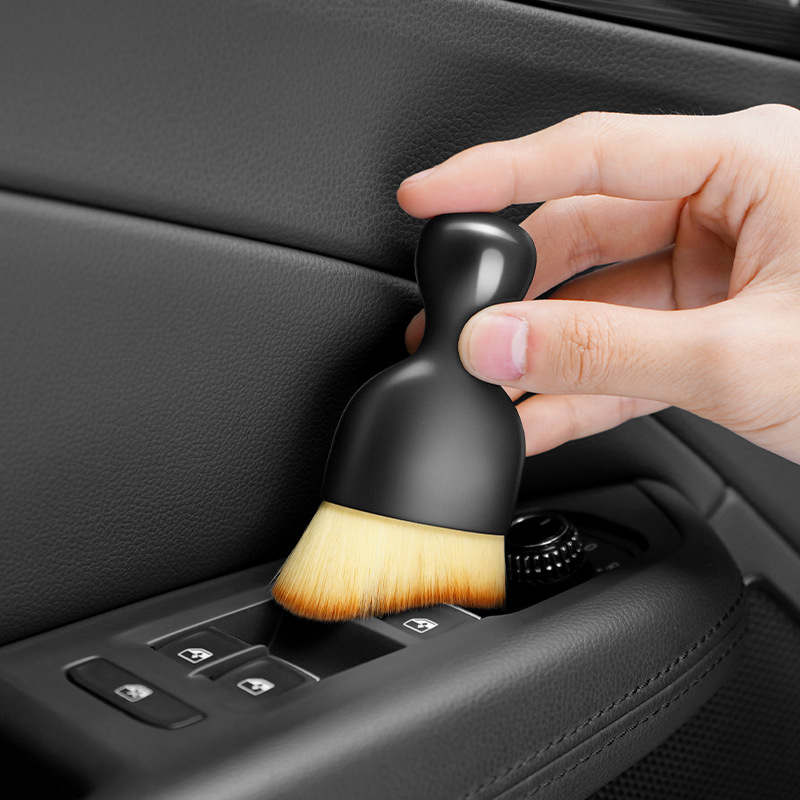 The gap brush in use: a hand sweeping the soft-bristled brush along the window-switch panel of a car door.